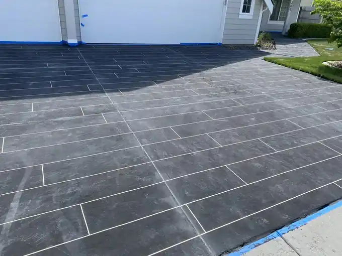Grey plank-pattern overlay on a driveway with blue tape along the siding and the pavement edge