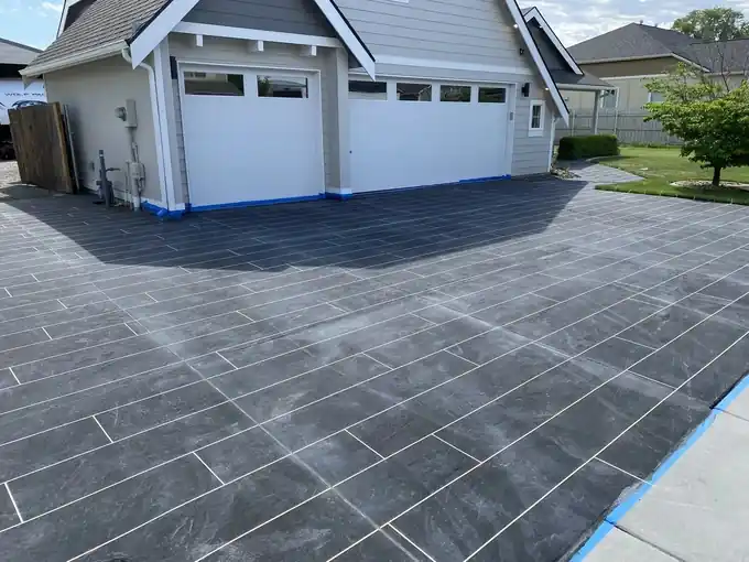 Plank-pattern concrete overlay on a driveway with blue tape at the garage and edges