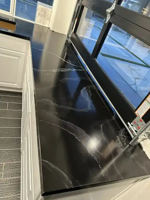 Long black metallic epoxy counter with pale veining beside white cabinets and a glass roll-up window