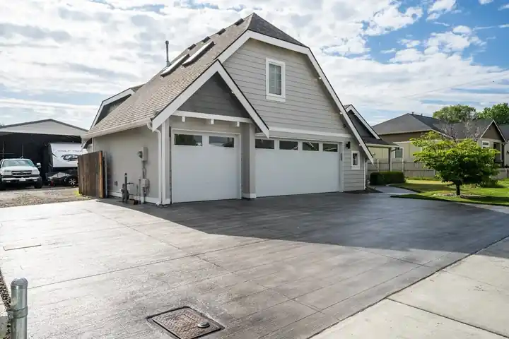 Finished dark stamped-plank driveway overlay in front of a grey house with white garage doors