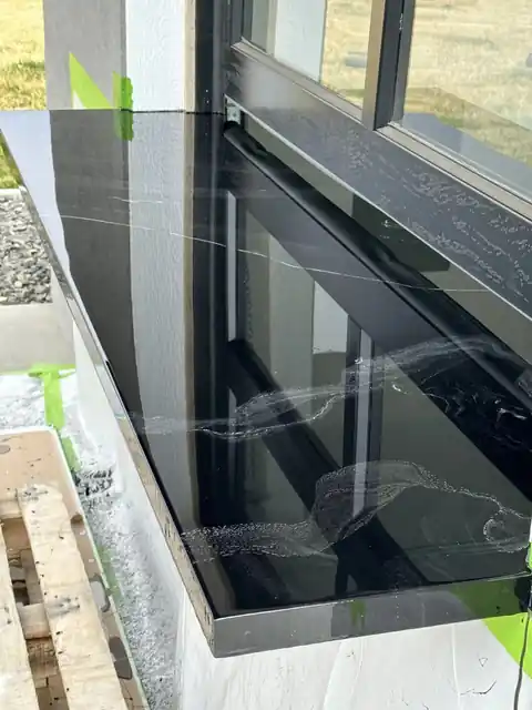 Glossy black epoxy counter edge at a window opening with green tape still on the wall