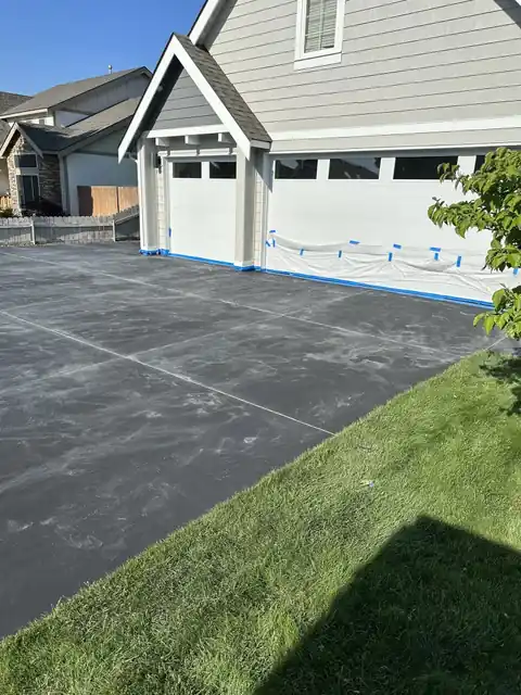 Dark overlay surface across a driveway in front of a two-car garage with blue tape along the garage edge