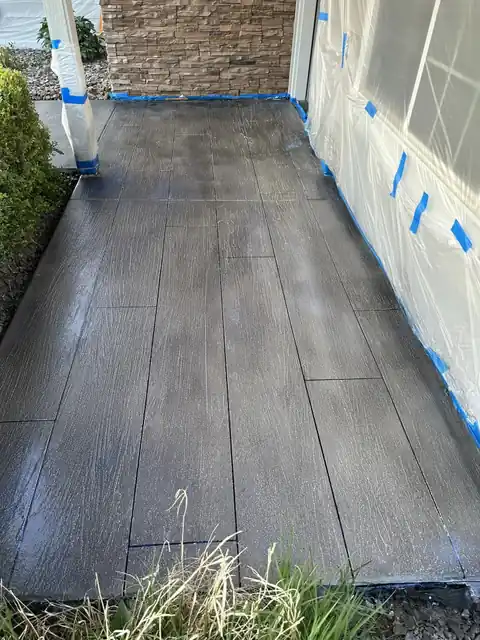 Stamped plank pattern on a porch slab with blue tape along the stone and siding edges