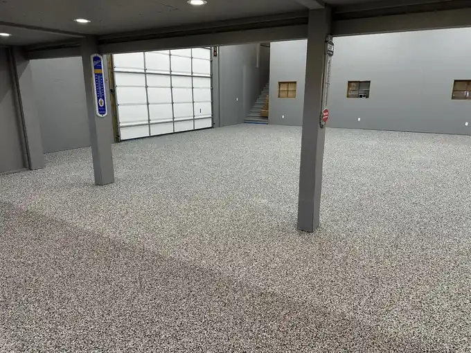 Speckled chip flake floor running between steel columns in an open building with a glass overhead door