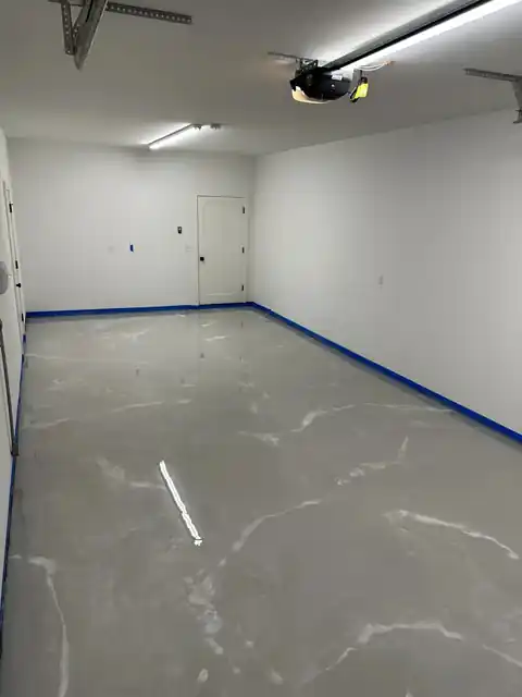 Glossy grey garage floor with pale streaks and blue tape along the base of the white walls