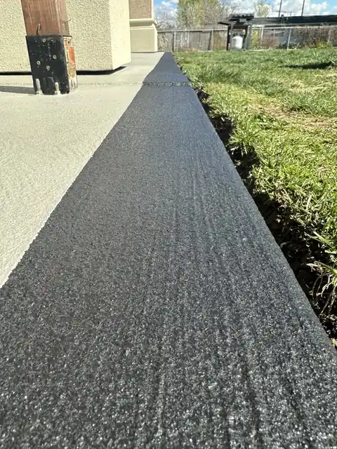 Narrow strip of dark textured overlay running along the edge of a lawn beside pale concrete